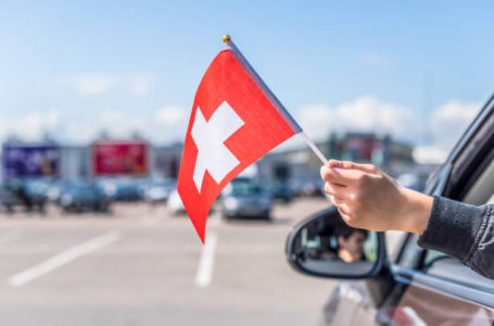 Boy holding Swiss Flag from the open car window on the parking of the shopping mall. Concept.  Switzerland