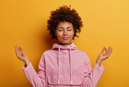 relieved-ethnic-woman-stands-lotus-pose-tries-meditate-during-quarantine-lockdown-reaches-nirvana-does-yoga-keeps-eyes-closed-dressed-sweatshirt-mental-health-relaxation-lifestyle-1-scaled-1.jpg